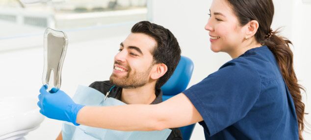 man-admiring-his-smile-in-mirror-sitting-next-to-dentist