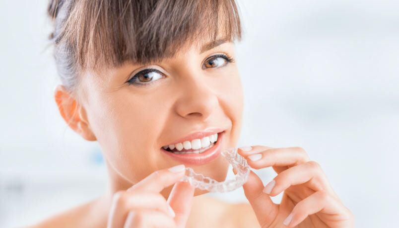 Smiling woman holding a custom mouthguard, highlighting bruxism treatment in Aurora, Ontario.